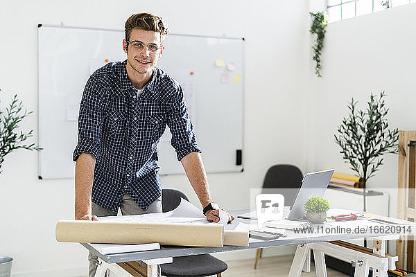 Smiling man leaning on desk while standing at office