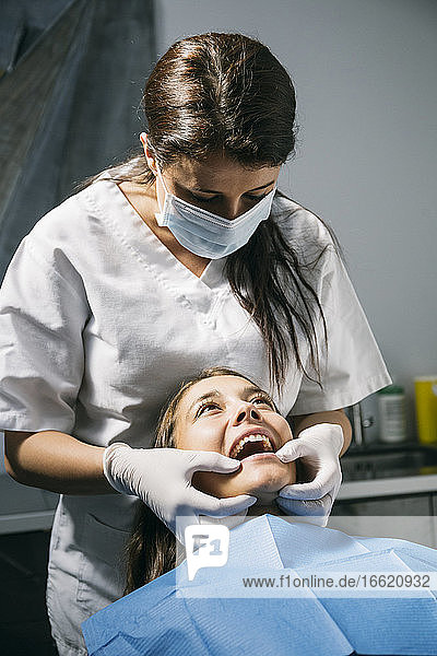 Weibliche Zahnarzthelferin mit Mundschutz und Handschuhen bei der Untersuchung der Mundhöhle eines Patienten