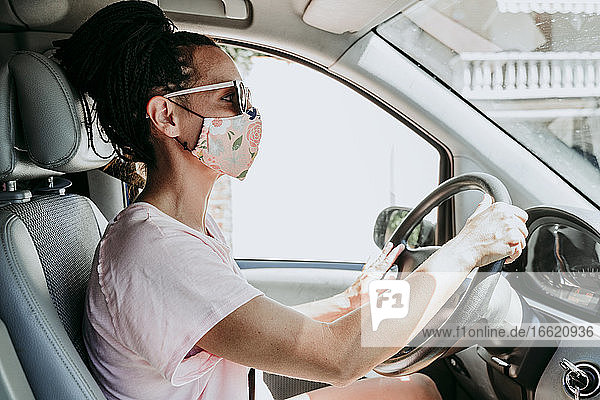 Frau mit Schutzmaske beim Autofahren in der Stadt an einem sonnigen Tag