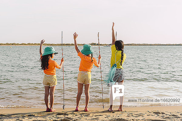 Freunde betrachten die Aussicht mit erhobener Hand am Strand stehend