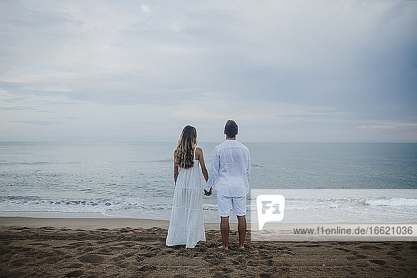 Paar hält sich an den Händen und bewundert die Aussicht auf das Meer am Strand