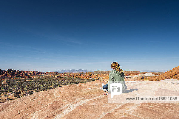 Frau sitzt auf einer Felsformation im Valley of Fire State Park vor blauem Himmel  Nevada  USA
