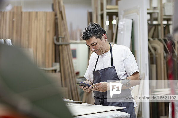 Männlicher Künstler  der ein Mobiltelefon benutzt  während er in einer Werkstatt steht