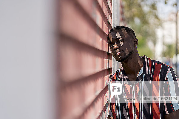 Young man in casuals leaning on fence outdoors