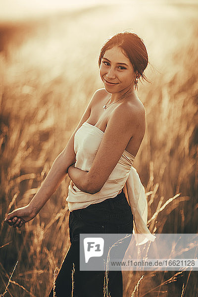 Young woman wearing off shoulder top standing in field at sunset