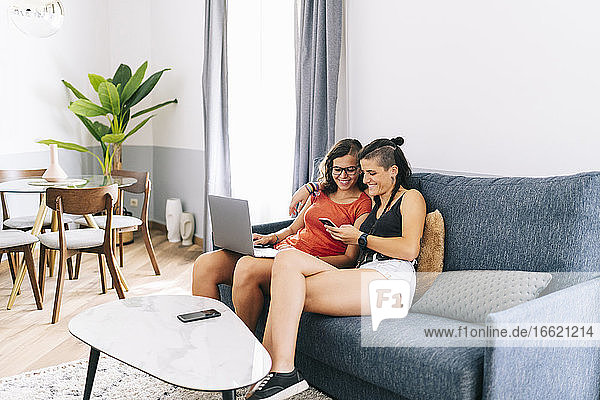 Freundinnen nutzen zu Hause Laptop und Textnachrichten auf dem Smartphone