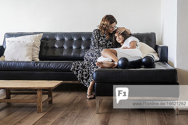 Mutter  die ihre Tochter umarmt  während sie sich zu Hause auf dem Sofa ausruht