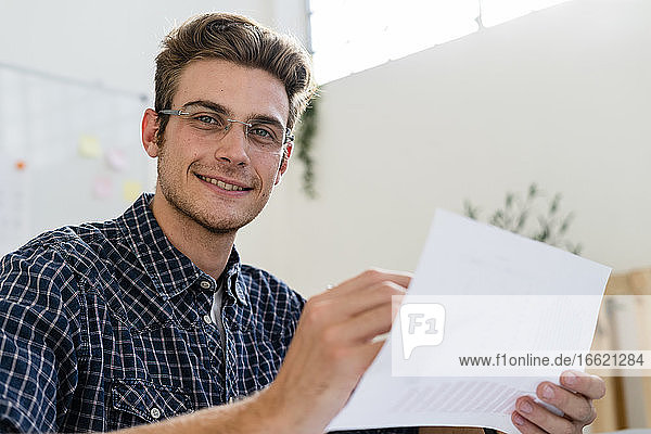 Lächelnder Mann hält Papier bei der Arbeit im Büro