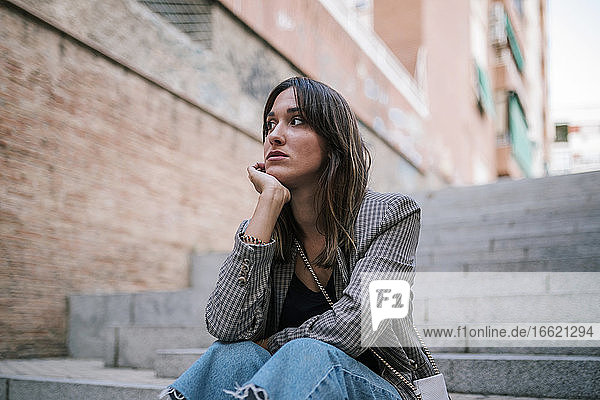 Thoughtful woman with hand on chin sitting outdoors