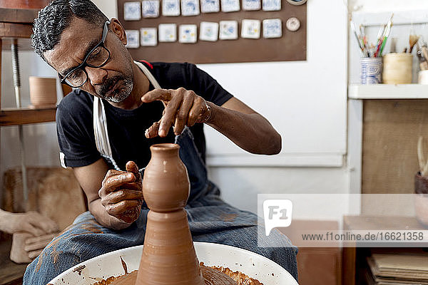Close-up of male potter making earthenware while sitting in workshop
