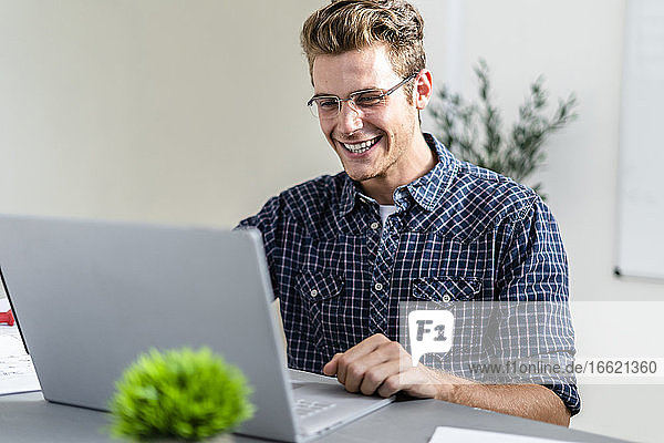 Lächelnder Mann  der einen Laptop benutzt  während er im Büro sitzt