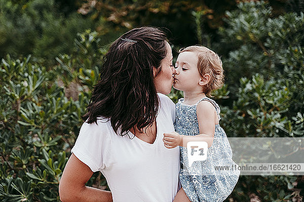 Happy mother and daughter kissing each other while standing in park