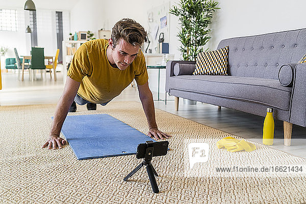 Young man looking at mobile phone while exercising on mat at home