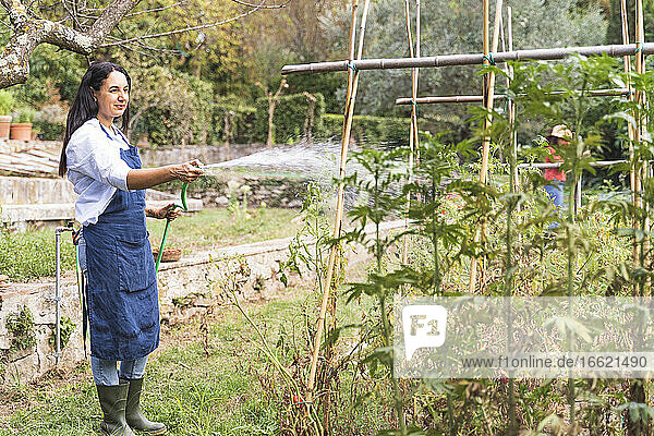 Frau bei der Gartenarbeit  während sie im Gemüsegarten Wasser aus dem Schlauch sprüht
