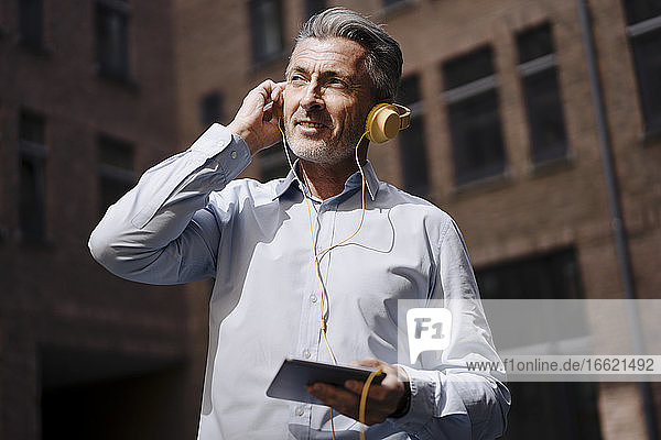 Businessman with headphones using phone while standing against building