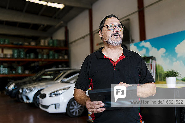 Mechaniker mit digitalem Tablet  der in der Werkstatt vor Autos steht