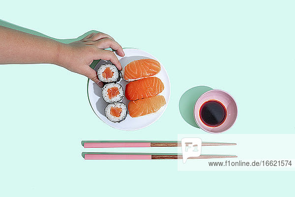 Hand of little girl picking up piece of maki sushi