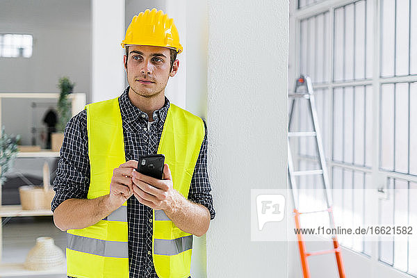 Architekt  der ein Mobiltelefon benutzt  während er in einem im Bau befindlichen Büro steht