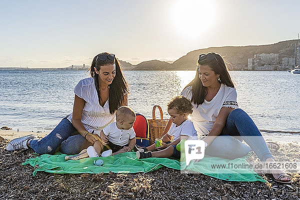 Schwestern mit Baby Söhne sitzen am Strand gegen den Himmel bei Sonnenuntergang