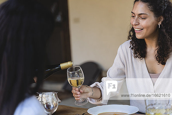 Lächelnde Frau hält ein Weinglas  während sie am Esstisch im Hinterhof sitzt