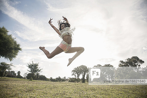 Junge Frau springt gegen den klaren Himmel in einem öffentlichen Park