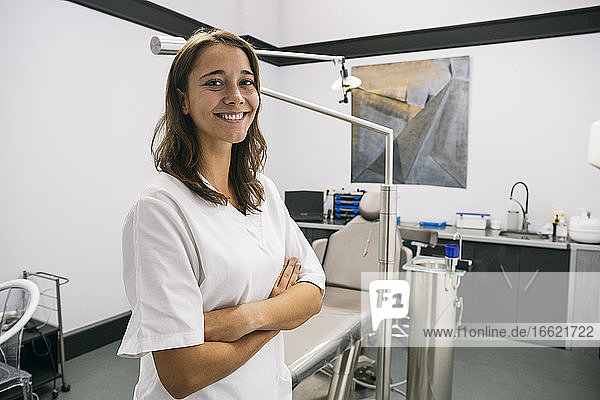 Confident female dentist assistant standing with arms crossed in clinic