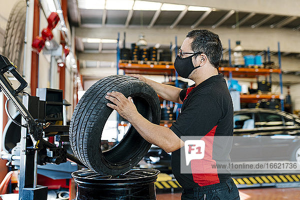 Mechanic wearing mask examining tire in auto repair shop