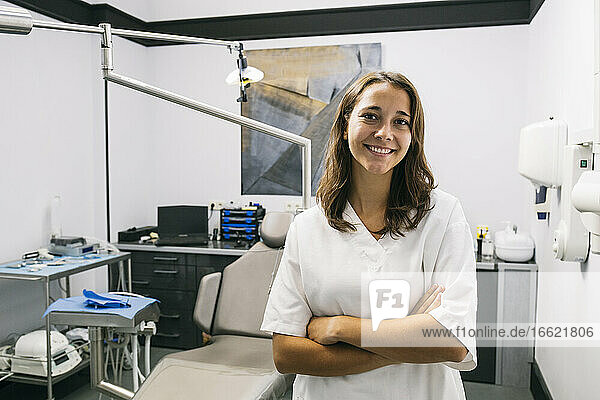Lächelnde Zahnarzthelferin mit verschränkten Armen im Büro stehend