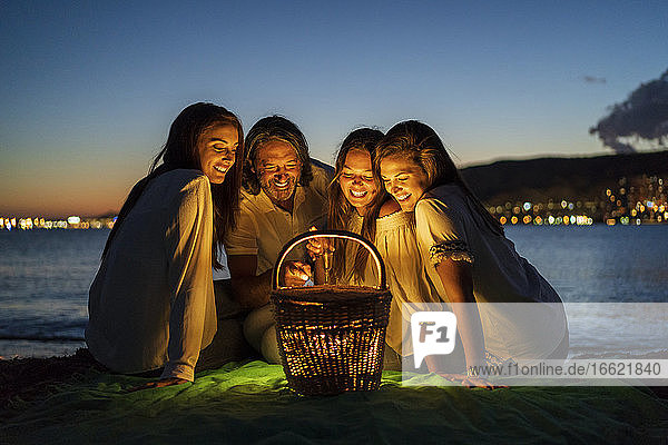 Mann mit Töchtern betrachtet beleuchteten Korb  während er in der Abenddämmerung am Meer sitzt