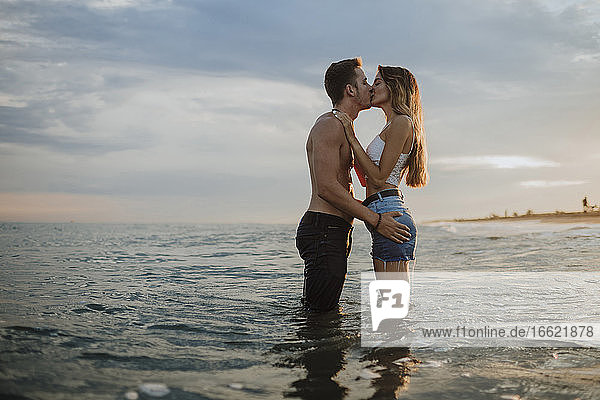 Couple kissing while standing in water at beach during sunset