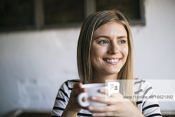 Lächelnde Frau schaut weg  während sie in einem Café Kaffee trinkt