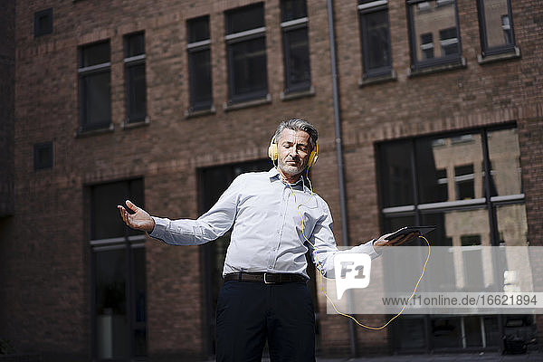 Geschäftsmann tanzt beim Hören von Musik gegen Gebäude