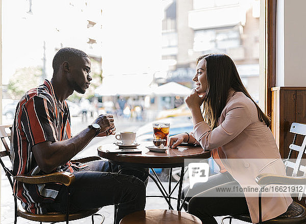 Lächelnde junge Frau im Gespräch mit ihrem Freund  während sie ihre Freizeit in einem Café verbringt