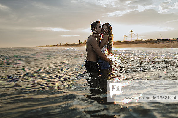Man kissing woman while standing in water at beach