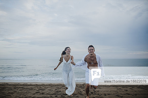 Happy couple holding hands while running on beach