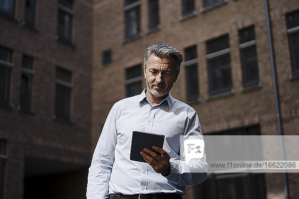 Geschäftsmann  der ein digitales Tablet hält  während er an einem Gebäude steht