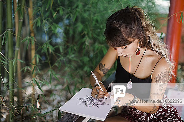 Frau  die im Park sitzend in einem Buch zeichnet