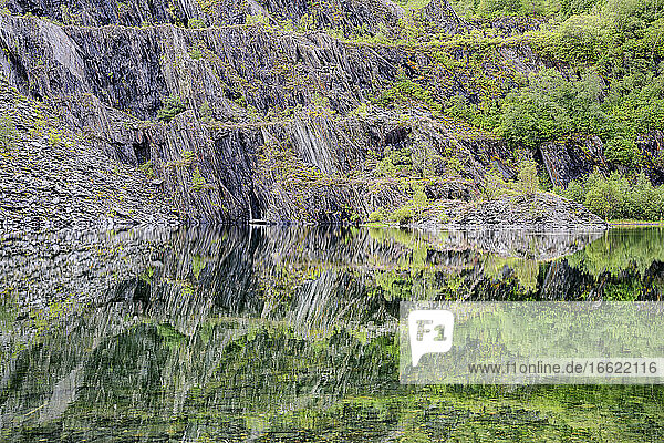 Schieferklippen spiegeln sich in einem klaren  glänzenden See in den schottischen Highlands