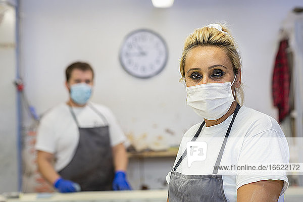 Mittlere erwachsene Frau mit Gesichtsmaske  die mit einem Mitarbeiter im Hintergrund in einer Werkstatt steht