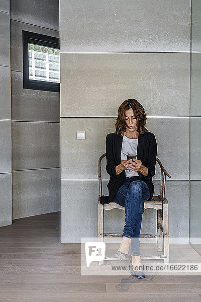 Frau  die ein Mobiltelefon benutzt  während sie auf einem Stuhl an der Wand im Büro sitzt