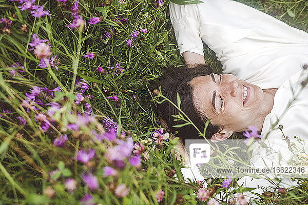 Fröhliche Frau mit geschlossenen Augen inmitten von Pflanzen an Land liegend