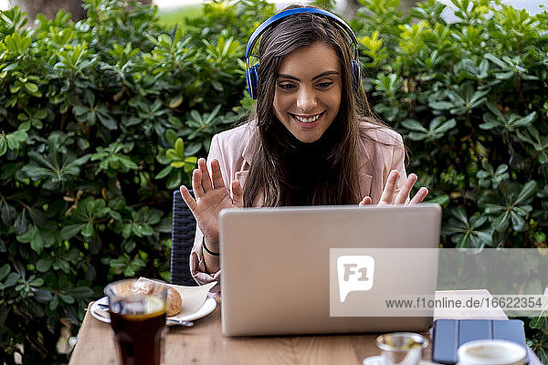 Lächelnde Unternehmerin  die mit ihrem Laptop Videogespräche führt  während sie auf der Terrasse eines Cafés sitzt