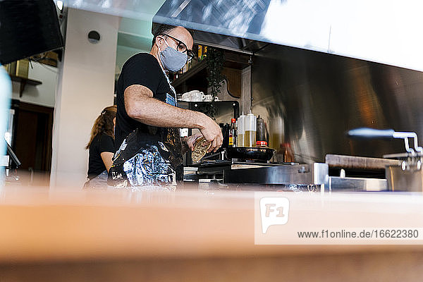 Männlicher Barista mit Gesichtsschutz beim Kochen in der Küche einer Kaffeebar während COVID-19