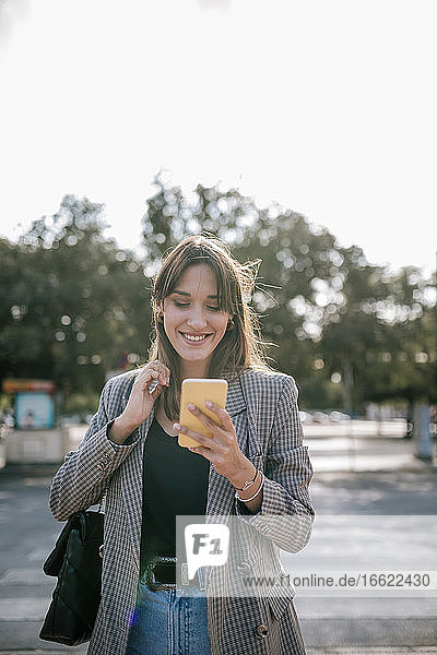 Lächelnde junge Frau  die ein Smartphone benutzt  während sie auf der Straße steht