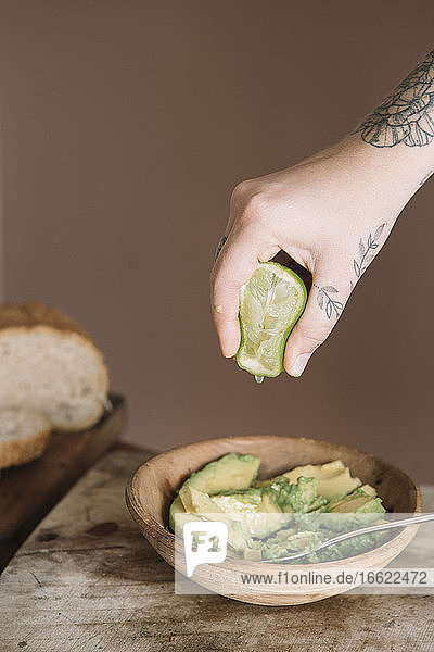 Frau drückt mit der Hand eine Limette in einen Avocadosalat  der auf einem Schneidebrett in der Küche aufbewahrt wird