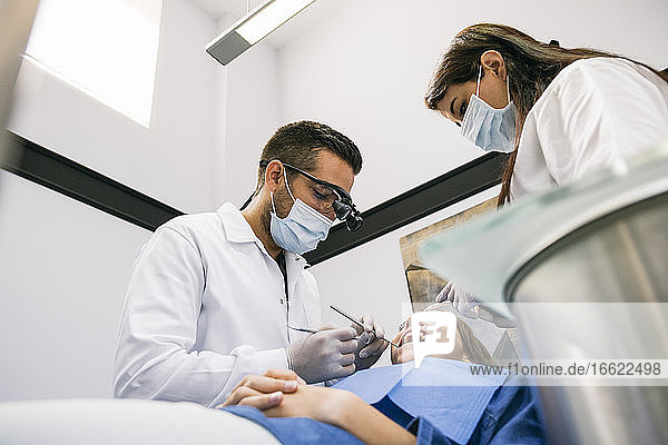 Arzt mit Hilfe einer Assistentin bei der Behandlung von Zahnkaries einer Patientin