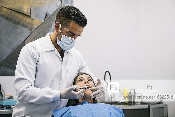 Ein männlicher Zahnarzt betäubt eine junge Patientin vor einer Zahnbehandlung in einer Klinik