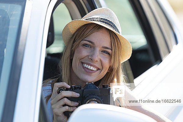 Lächelnde junge Frau  die eine Kamera hält  während sie im Auto sitzt