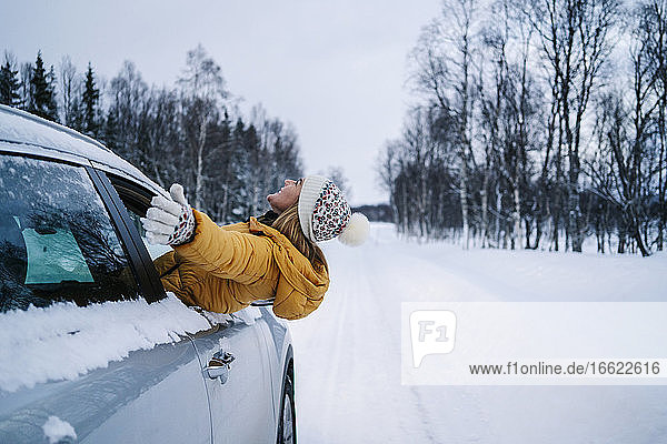Carefree woman with arms outstretched peeking through car window during winter