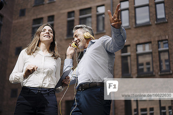 Lächelnde Kollegen hören Musik und tanzen gegen ein Gebäude